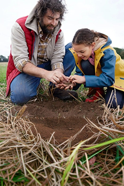 Un agricultor y una niña revisan la tierra de un campo