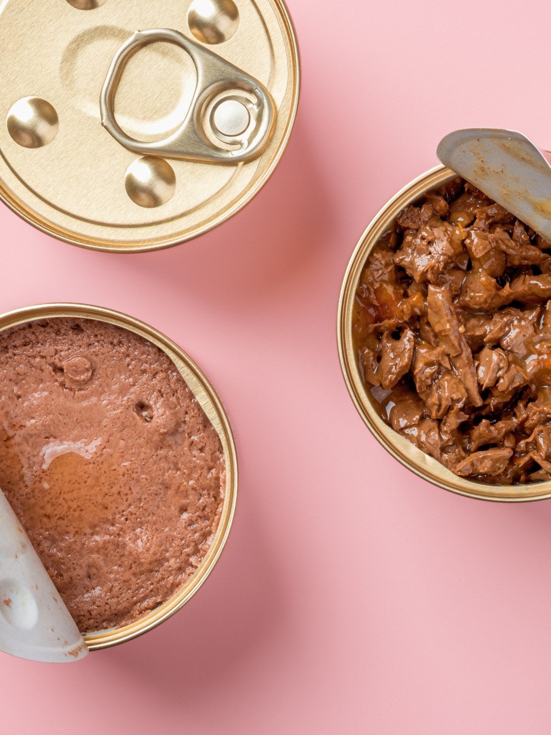 Latas abiertas de alimento húmedo para mascotas sobre un fondo rosa