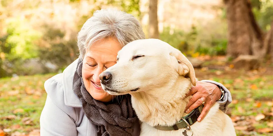 Mujer rubia que sabe cómo cuidar a un perro senior abrazando a su mascota.